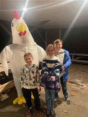 photo of three children in sweatshirts and coats standing beside a giant inflatable chicken