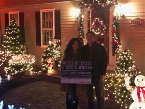 image of two people holding a sign in front of a house with lights and decorations